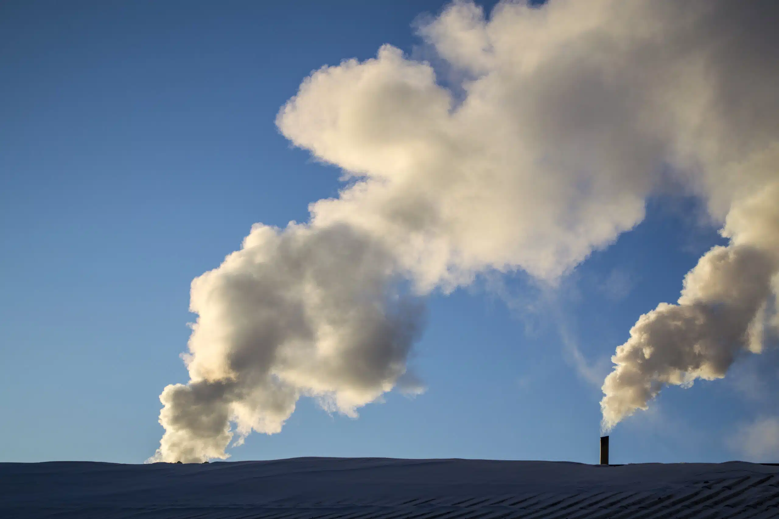 Exhaust plumes from industrial chimneys against a blue sky